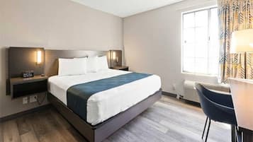 A hotel room with a bed, bedside tables, a desk, and a window.