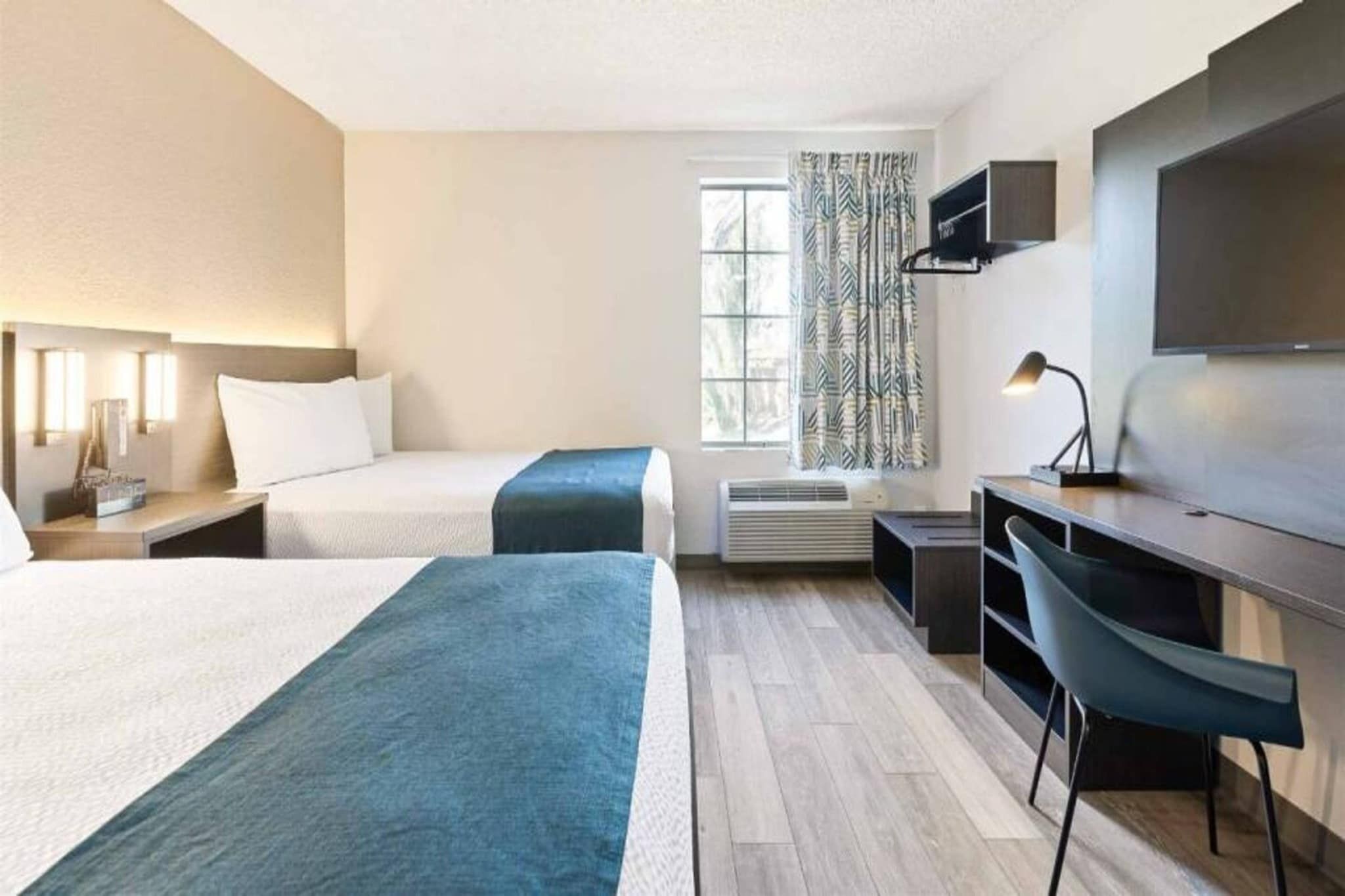 Ein Hotelzimmer mit zwei Betten, einem Schreibtisch, einem Sessel, einem Fernseher und einem Fenster mit Vorhängen.