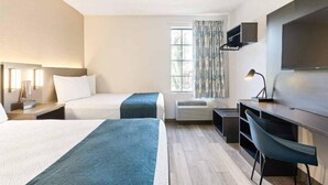 Ein Hotelzimmer mit zwei Betten, einem Schreibtisch, einem Sessel, einem Fernseher und einem Fenster mit Vorhängen.
