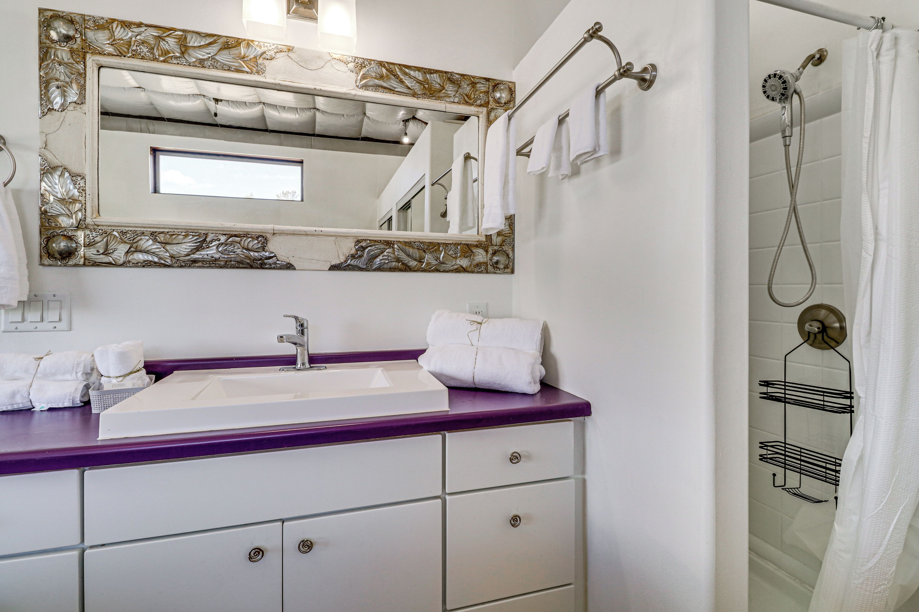 A bathroom with a white sink, purple countertop, and a shower with a glass door.