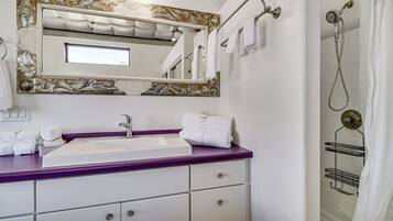A bathroom with a white sink, purple countertop, and a shower with a glass door.