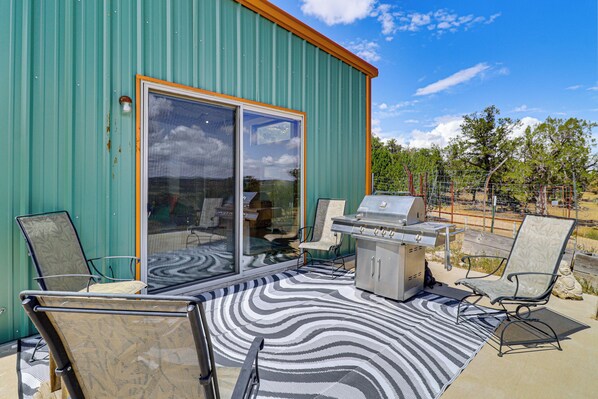 A patio with a grill and chairs, a patterned rug, and a sliding glass door.