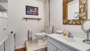 Casa de banho com sanita, lavatório, espelho e prateleira com uma fotografia sobre a sanita.
