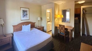 A hotel room with a bed, a desk, a chair, a mirror, and a wardrobe. - 1 King Bed | Non-Smoking, Micfridge (Tempe)