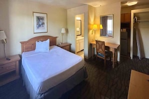 Una habitación de hotel con cama, escritorio, silla, espejo y armario.