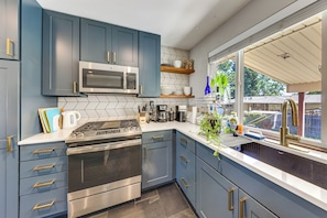 A modern kitchen with blue cabinets, stainless steel appliances, and a window with a view of the outdoors. - 8 Mi to Red Rocks! Quiet Home w/ Patio & Yard (Lakewood)