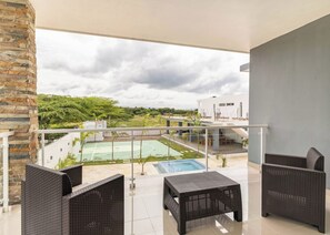 A balcony with wicker furniture, a pool, and a view of a sports court and greenery. - 10BR Luxury Villa  Private Pool (Sosúa)