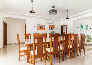 A dining area with a long wooden table and chairs, an air conditioning unit, and wall-mounted artwork. - 10BR Luxury Villa  Private Pool (Sosúa)