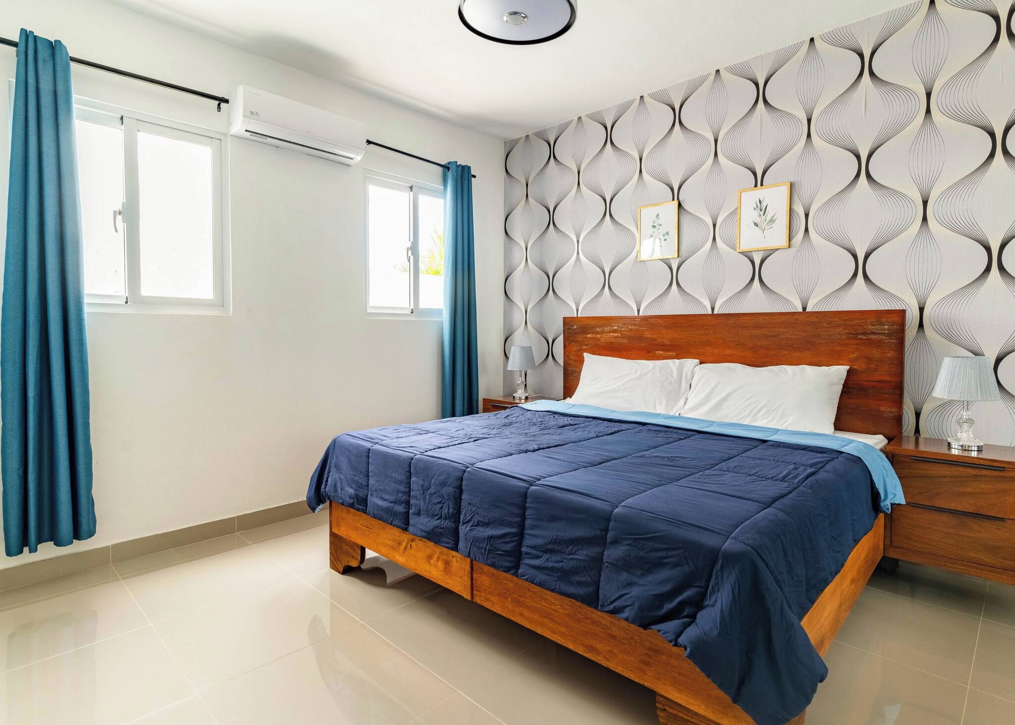 Un dormitorio con una cama de madera, una mesita de noche, un aire acondicionado de pared y una ventana con cortinas.