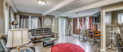 A spacious living room with a leather sofa, a glass coffee table, and a red rug.