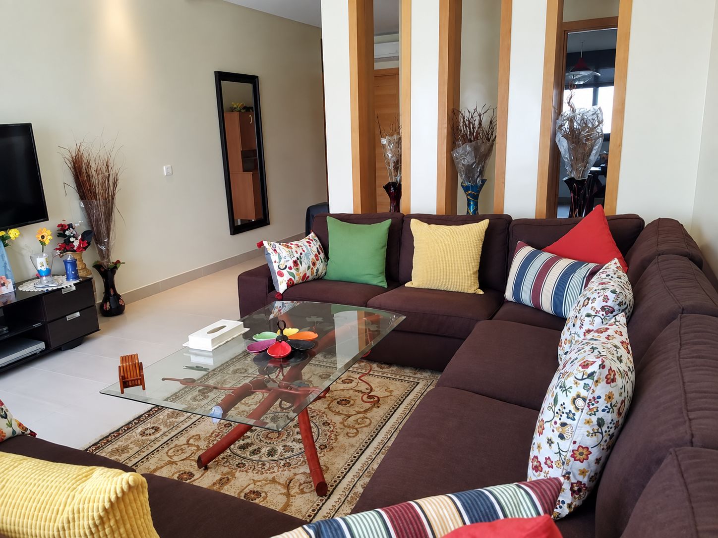 Un salon moderne avec un canapé d’angle, une table basse en verre et des coussins décoratifs.