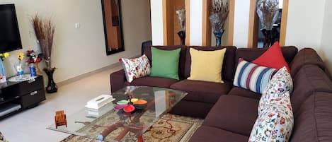 A modern living room with a sectional sofa, a glass coffee table, and decorative pillows.