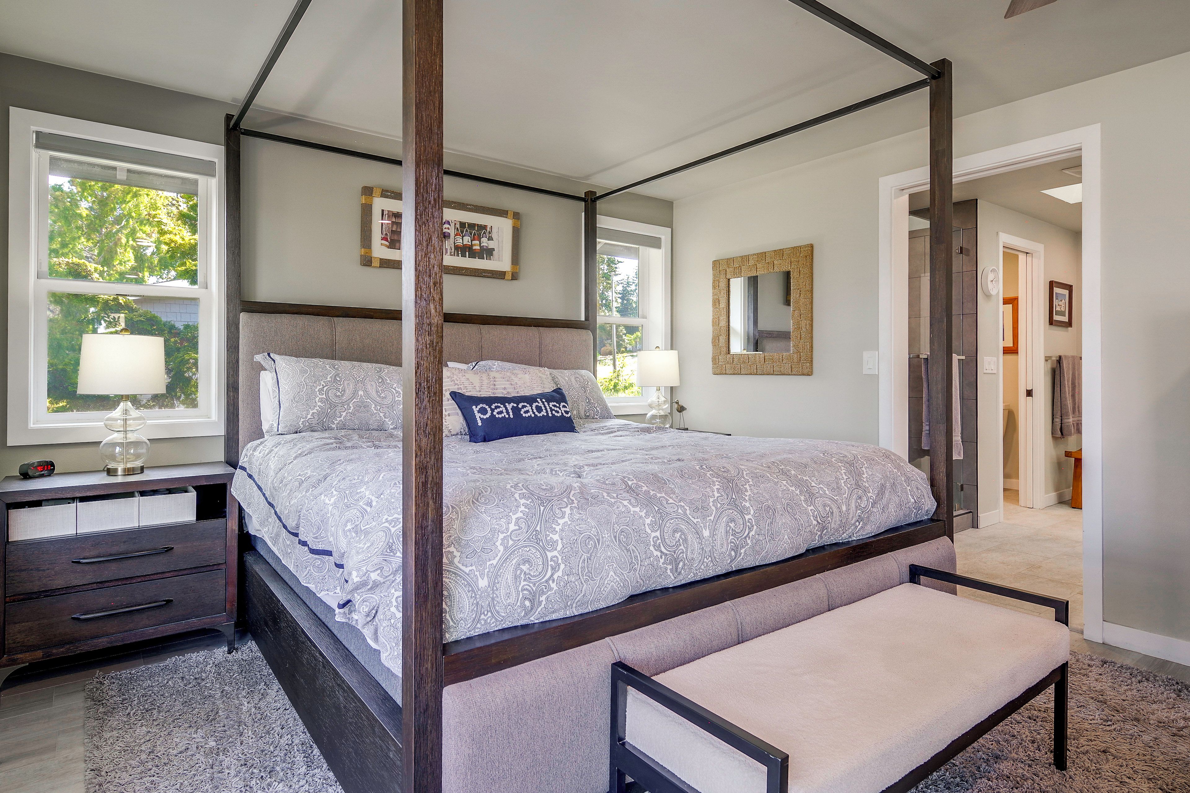 A four-poster bed with a bench, bedside tables, and a view of the outdoors through large windows.