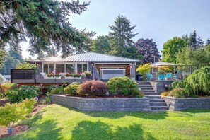 Une maison moderne dotée d’un patio couvert, d’un jardin devant la maison agrémenté de diverses plantes et d’un escalier menant à l’entrée.