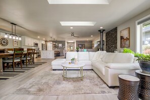 A modern living room with a white sofa, a dining area with wooden chairs, and a kitchen in the background. - Waterfront Whidbey Island Oasis! Hot Tub + Patio (Freeland)