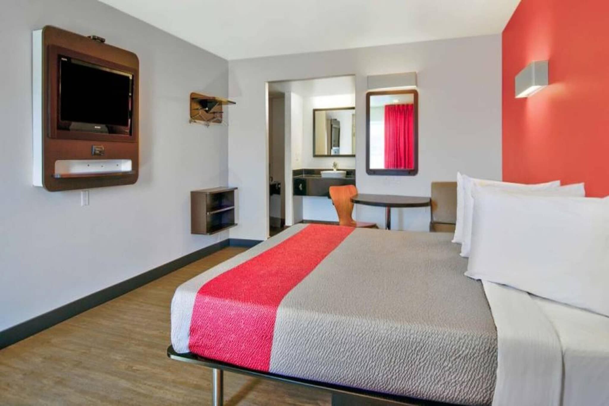 Habitació d'hotel amb un llit, televisió, escriptori i un bany visible a través d'una porta oberta.