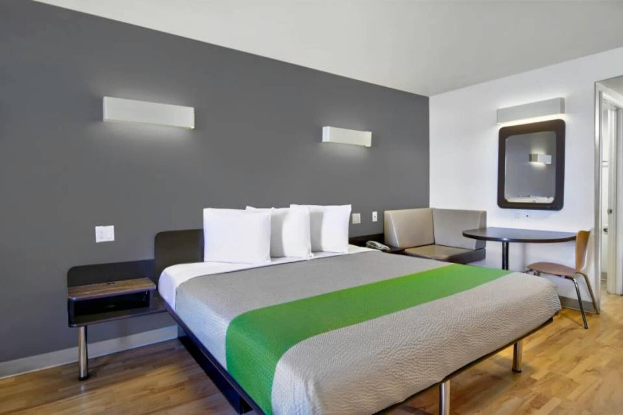A hotel room with a bed, bedside table, chair, desk, and a mirror.
