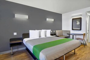 Una habitación de hotel con cama, mesita de noche, silla, escritorio y espejo.