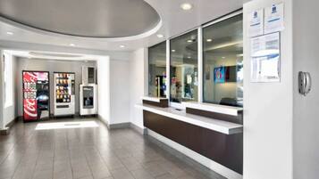A modern reception area with a counter, vending machines, and a glass door leading to the interior.