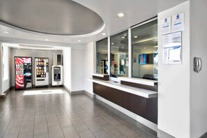 Een moderne receptiezone met een balie, automaten en een glazen deur naar de binnenruimte.