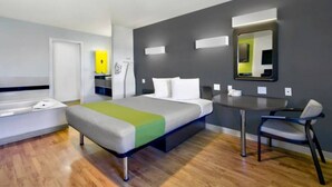 A modern hotel room with a bed, bedside table, chair, and a small desk with a mirror. - 1 King Bed|Smoking|Victorville (VICTORVILLE)