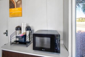 A microwave on a countertop with a coffee maker and cups. - 1 King Bed|Smoking|Victorville (VICTORVILLE)