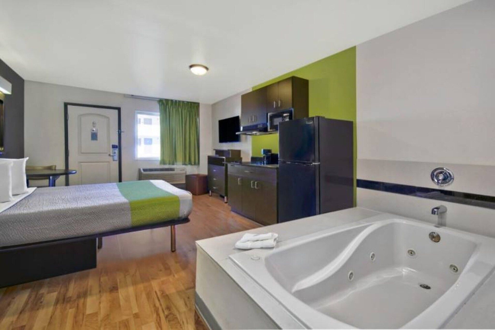 Habitación de hotel con cama, una mesita, kitchenette y bañera.