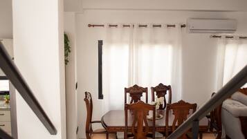A staircase leading to a dining area with wooden chairs and a table, an air conditioning unit on the wall, and a ceiling light fixture.