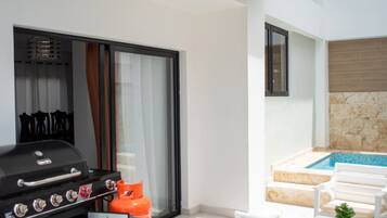 A modern outdoor patio with a barbecue grill, a gas cylinder, white outdoor furniture, and a swimming pool.
