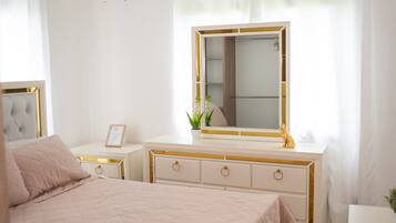 A bedroom with a bed, a vanity with a mirror, a ceiling fan, an air conditioning unit, and a window with curtains.