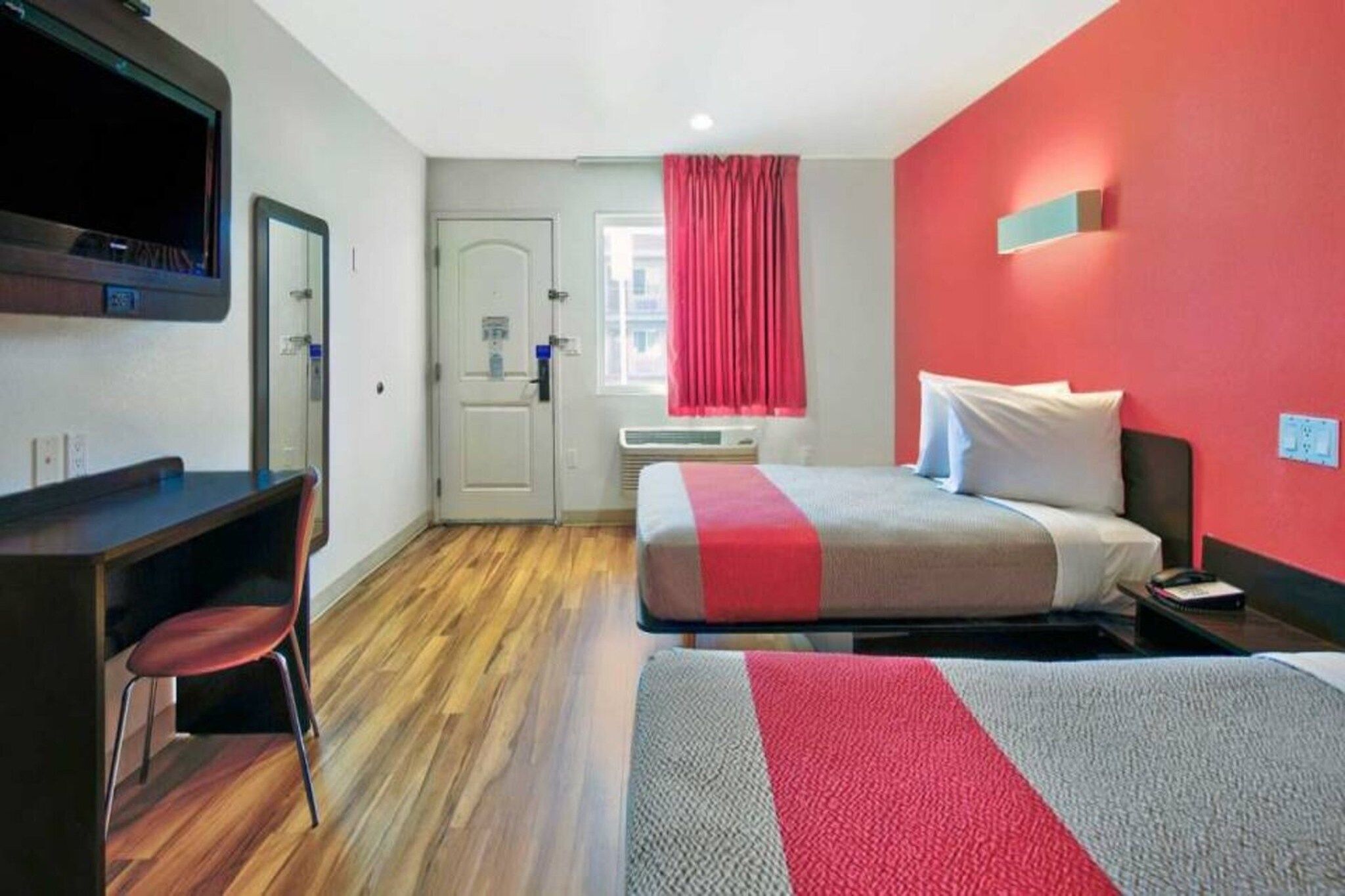 A hotel room with a bed, a desk, a chair, a television, and a window with curtains.