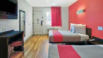 A hotel room with a bed, a desk, a chair, a television, and a window with curtains.
