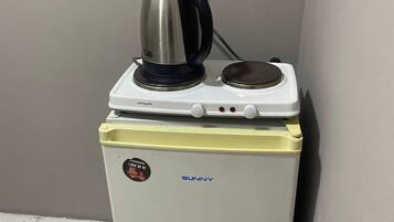 A compact refrigerator with a kettle on top, a power outlet on the wall, and a sticker with a phone number.