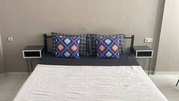 Ein Bett mit einem gemusterten Überwurf, zwei Kissen mit geometrischen Mustern und zwei Nachttische mit Lautsprechern.