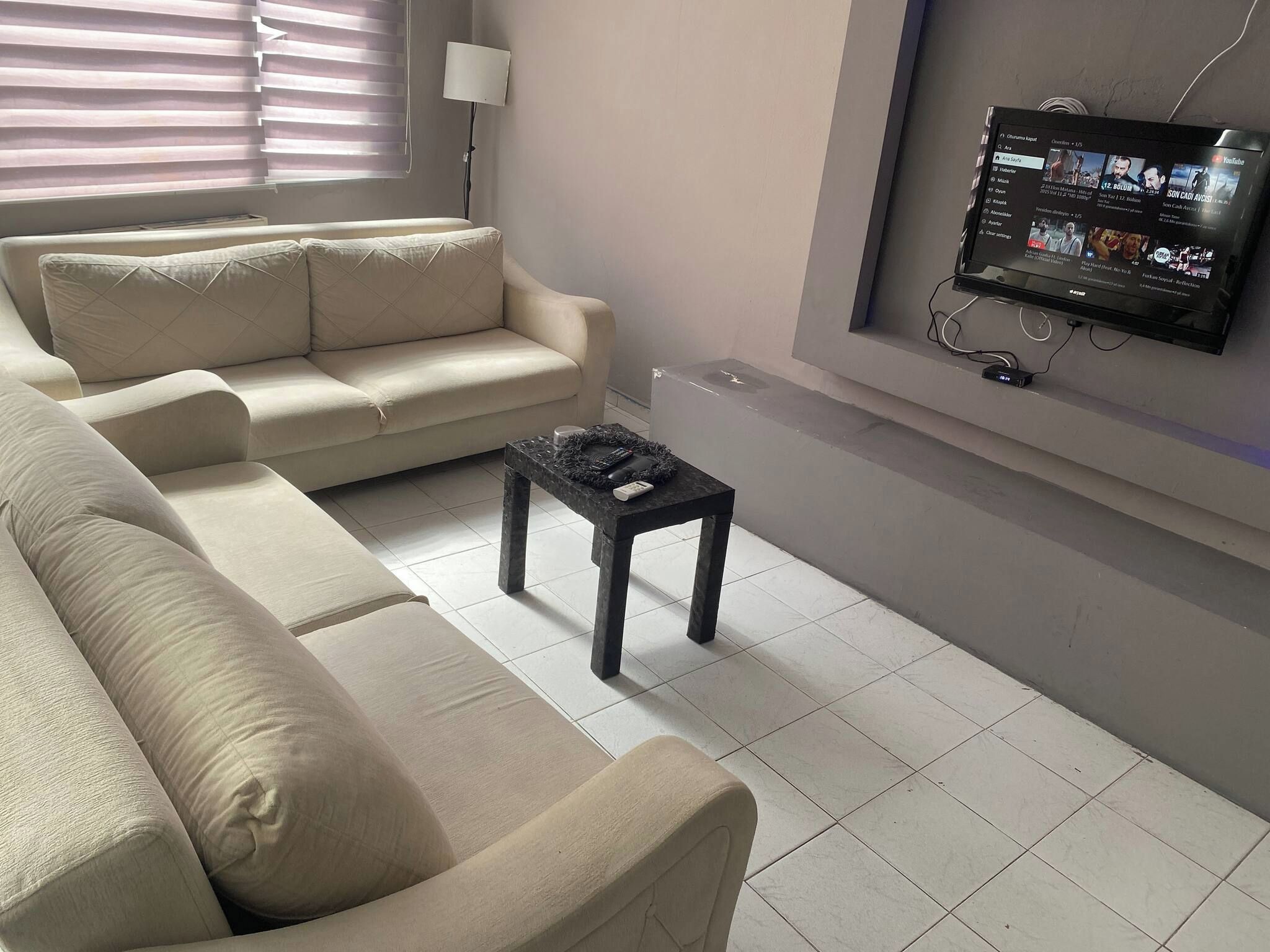 Ein Wohnzimmer mit einem beigen Sofa, einem kleinen schwarzen Tisch und einem an der Wand montierten Fernseher, der YouTube-Inhalte anzeigt.