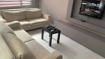 Ein Wohnzimmer mit einem beigen Sofa, einem kleinen schwarzen Tisch und einem an der Wand montierten Fernseher, der YouTube-Inhalte anzeigt.