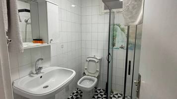 Ein Badezimmer mit weißem Waschbecken, WC und Dusche. Der Boden weist ein schwarz-weißes geometrisches Muster auf.