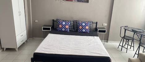 Een slaapkamer met een bed, nachtkastjes, een kledingkast, een klein tafeltje met stoelen en twee schilderijen aan de muur.