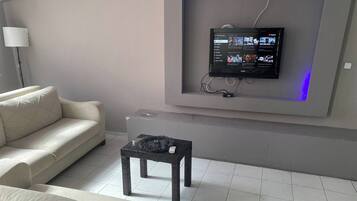 Ein modernes Wohnzimmer mit einem flachbildfernseher an der Wand, einem Sofa und einem kleinen Tisch mit einer Fernbedienung.