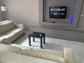 Ein modernes Wohnzimmer mit einem flachbildfernseher an der Wand, einem Sofa und einem kleinen Tisch mit einer Fernbedienung.