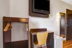 A hotel room with a desk, a chair, a television mounted on the wall, and a door.