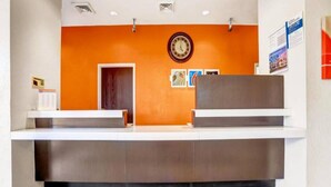 A reception desk with a clock above it, a door to the left, and a bulletin board with papers to the right. - 1 QUEEN BED | NON-SMOKING (Benson)