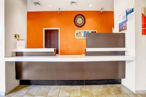 Un mostrador de recepción con un reloj encima, una puerta a la izquierda y un tablón de anuncios con papeles a la derecha.