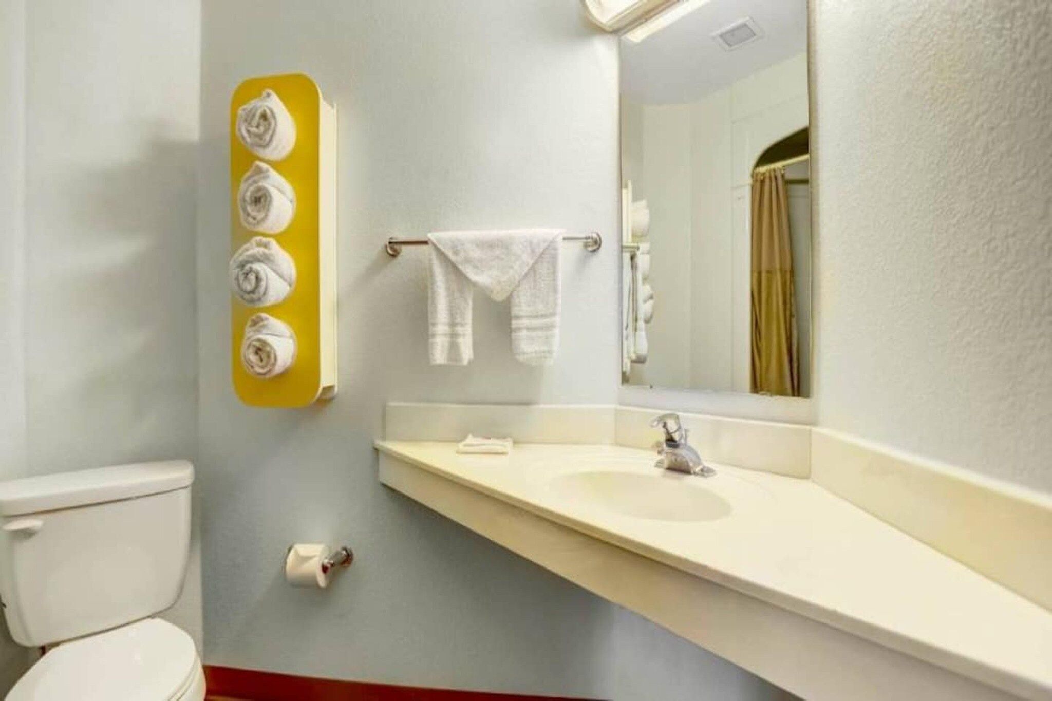 Ein Badezimmer mit Toilette, Waschbecken, Spiegel, Handtuchhalter und einer Toilettenpapierrolle.