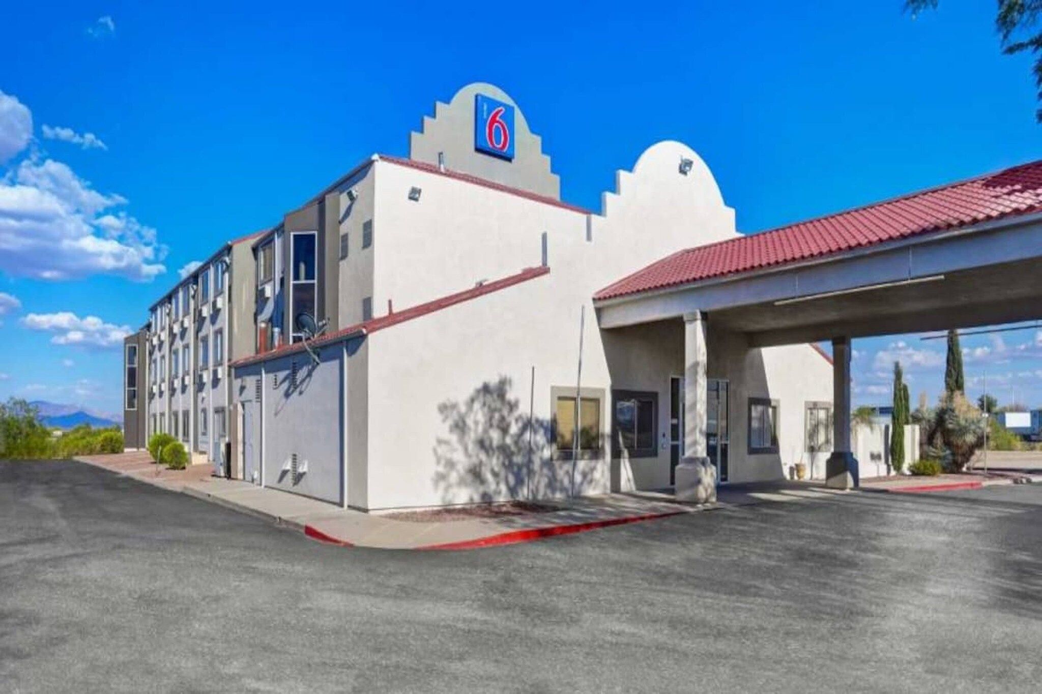 A 6-story motel with a red roof, a covered parking area, and a clear blue sky.