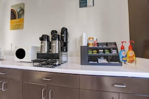 Mostrador de habitaciones de hotel con cafetera, dispensador de agua y un refrigerador pequeño.