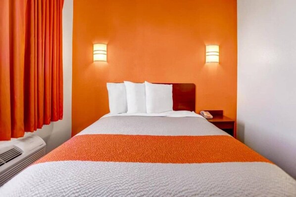 A hotel room with a bed, white pillows, an orange-striped blanket, a nightstand, and two wall-mounted lights.