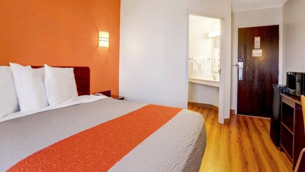 A hotel room with a bed, a desk, a microwave, and a door leading to a bathroom. - 1 QUEEN BED | NON-SMOKING (Benson)