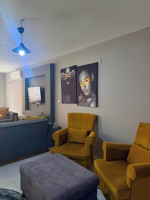 A modern living room with a blue ceiling light, two mustard-colored armchairs, a gray ottoman, and two abstract paintings on the wall. - 2-Bedroom Apartment in Central Pendik, Turkey (Pendik)