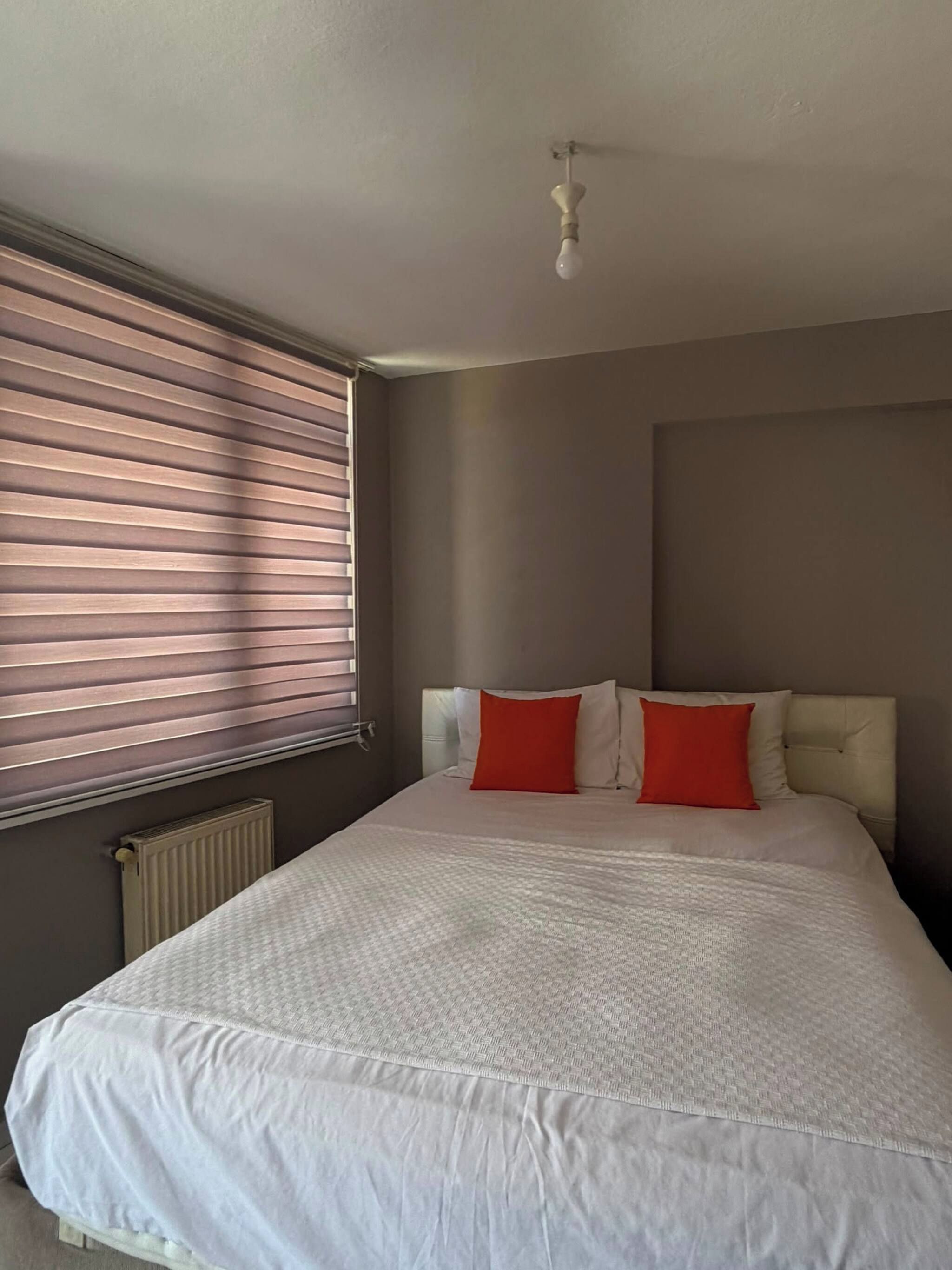 Ein Schlafzimmer mit einem großen Bett, einem Heizkörper und einem Fenster mit Jalousien.